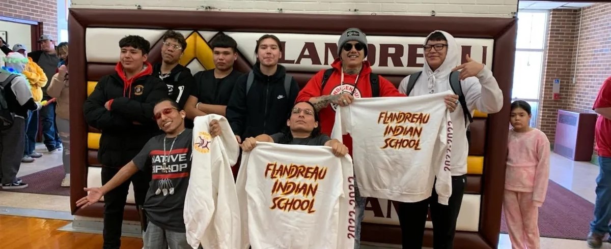 Large group of students in school holding up white sweatshirts with school name on front.