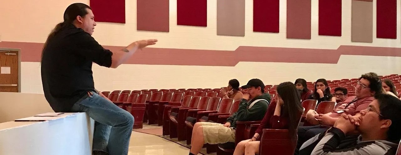 Instructor speaks to group of students in the school auditorium.