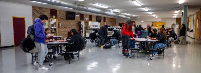 High school students enjoy lunch together in the bustling cafeteria, surrounded by tables and food trays.
