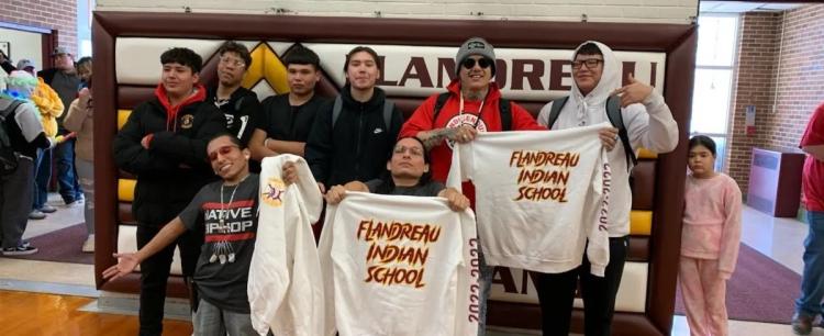 Large group of students in school holding up white sweatshirts with school name on front.